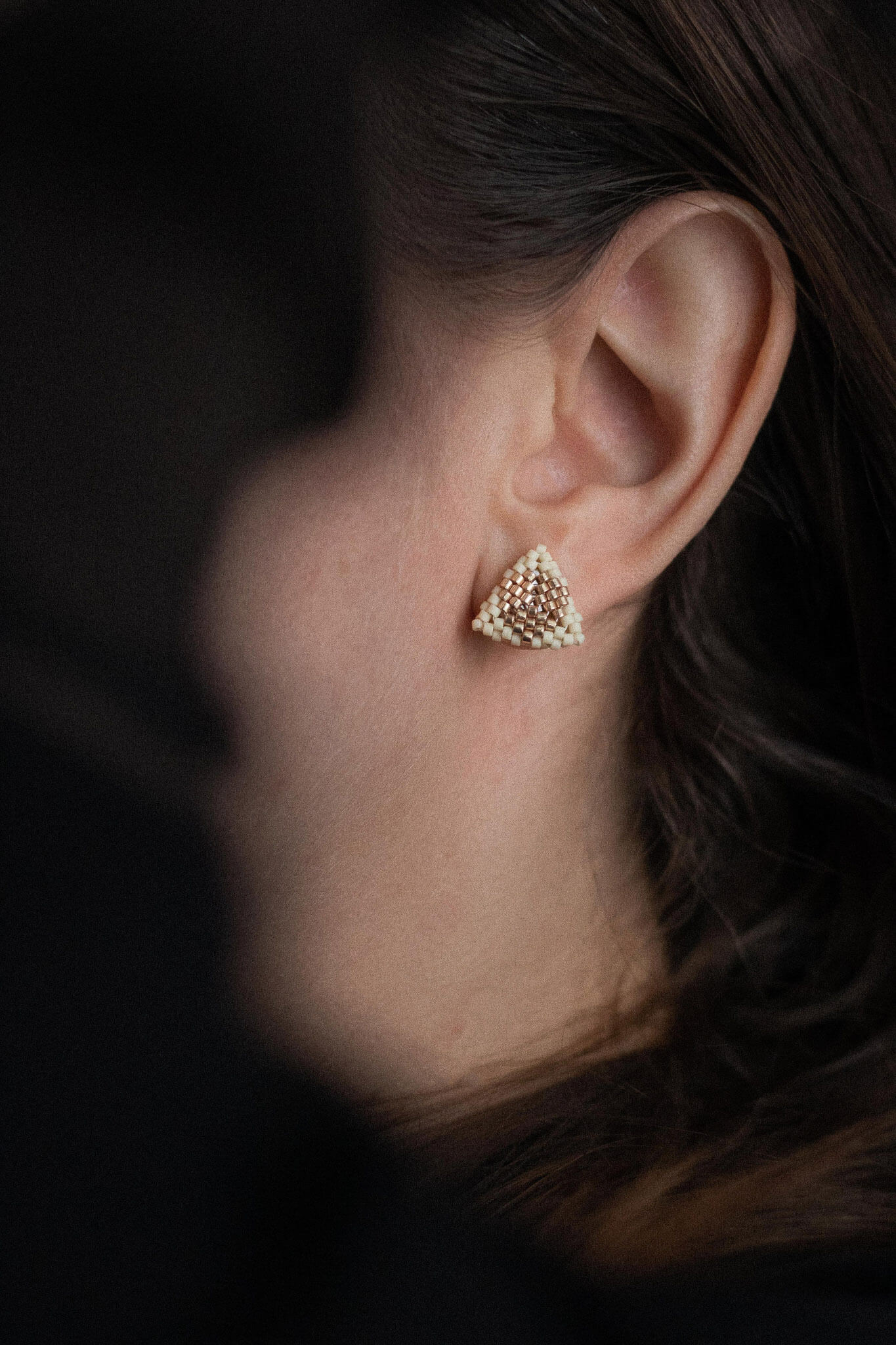 Greige beaded triangle stud earrings with metallic center detail, greige beads, worn on the ear.