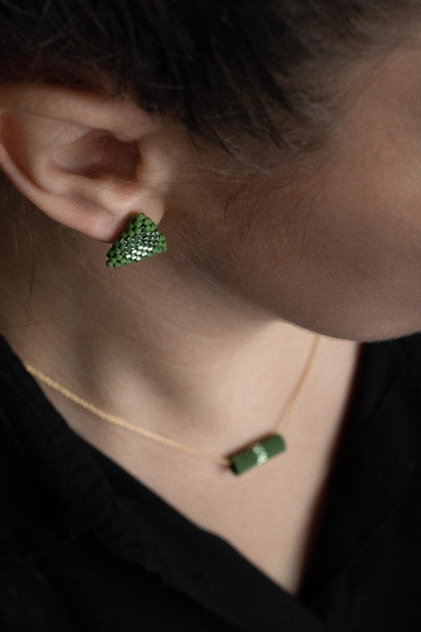 Green beaded triangle stud earrings with metallic center detail, moss green beads, worn on the ear.
