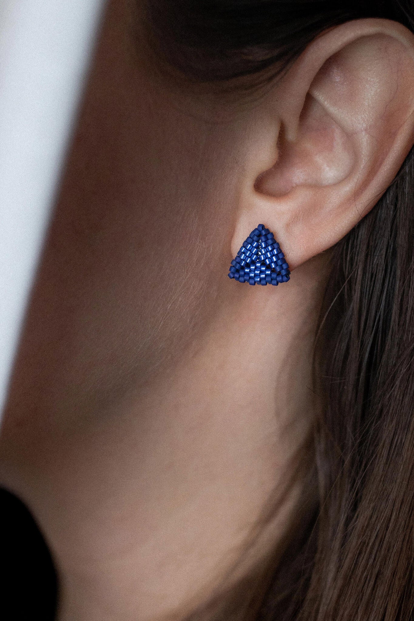Blue beaded triangle stud earrings with metallic center detail, royal blue beads, worn on the ear.