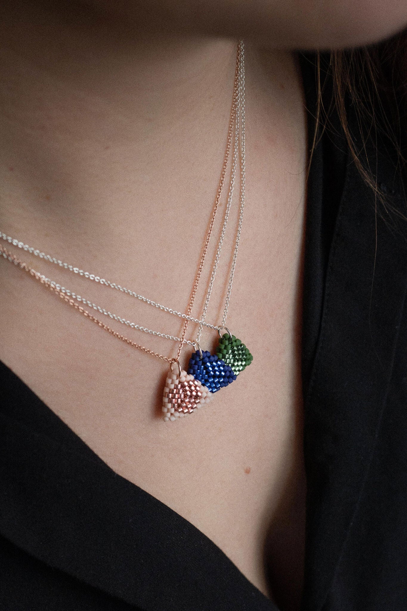 Three beaded triangle pendant necklaces in pink, blue and green tones, on silver and rose gold chains, worn layered on neck.
