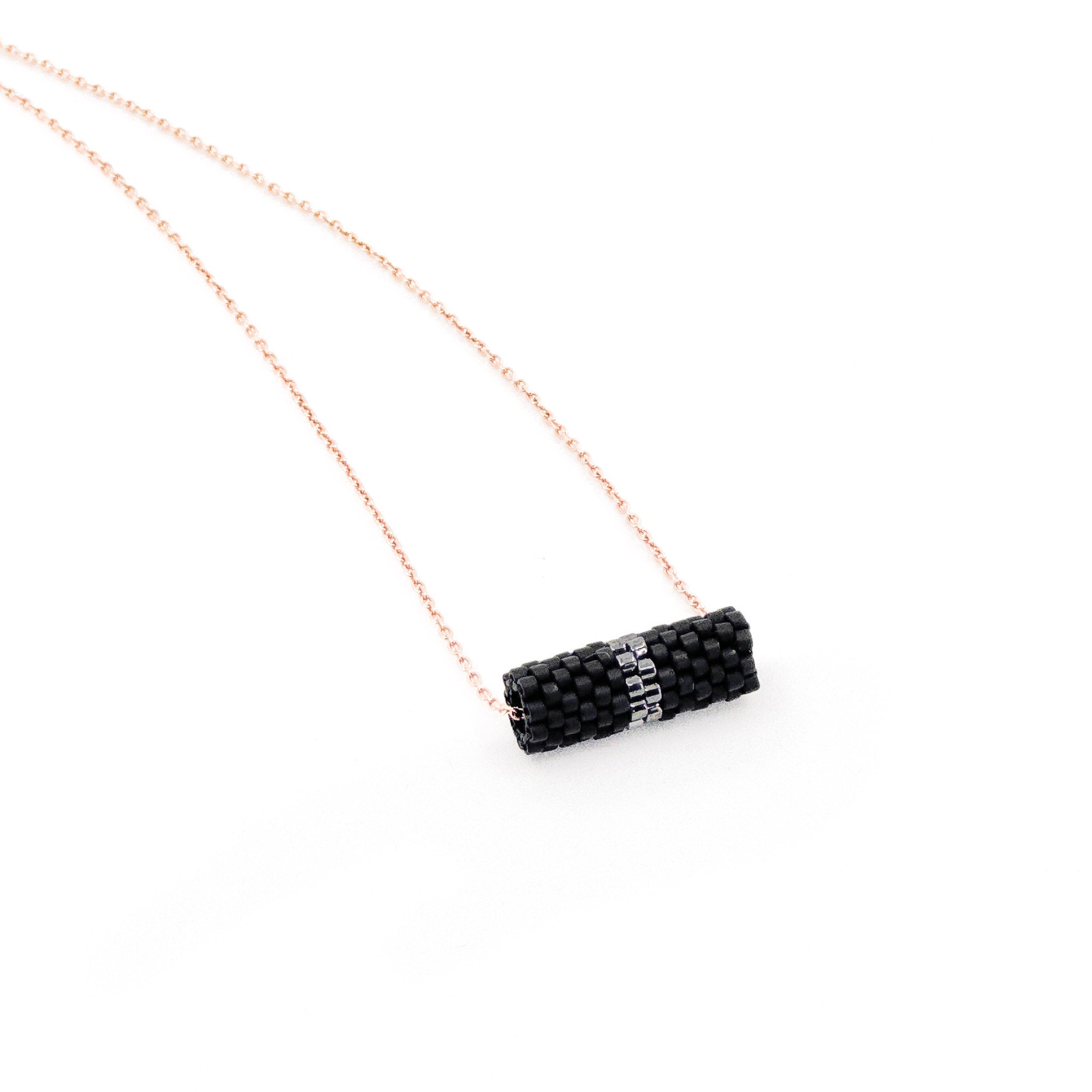 Black beaded tube pendant necklace with rose gold chain and metallic center detail, charcoal black beads, side view.