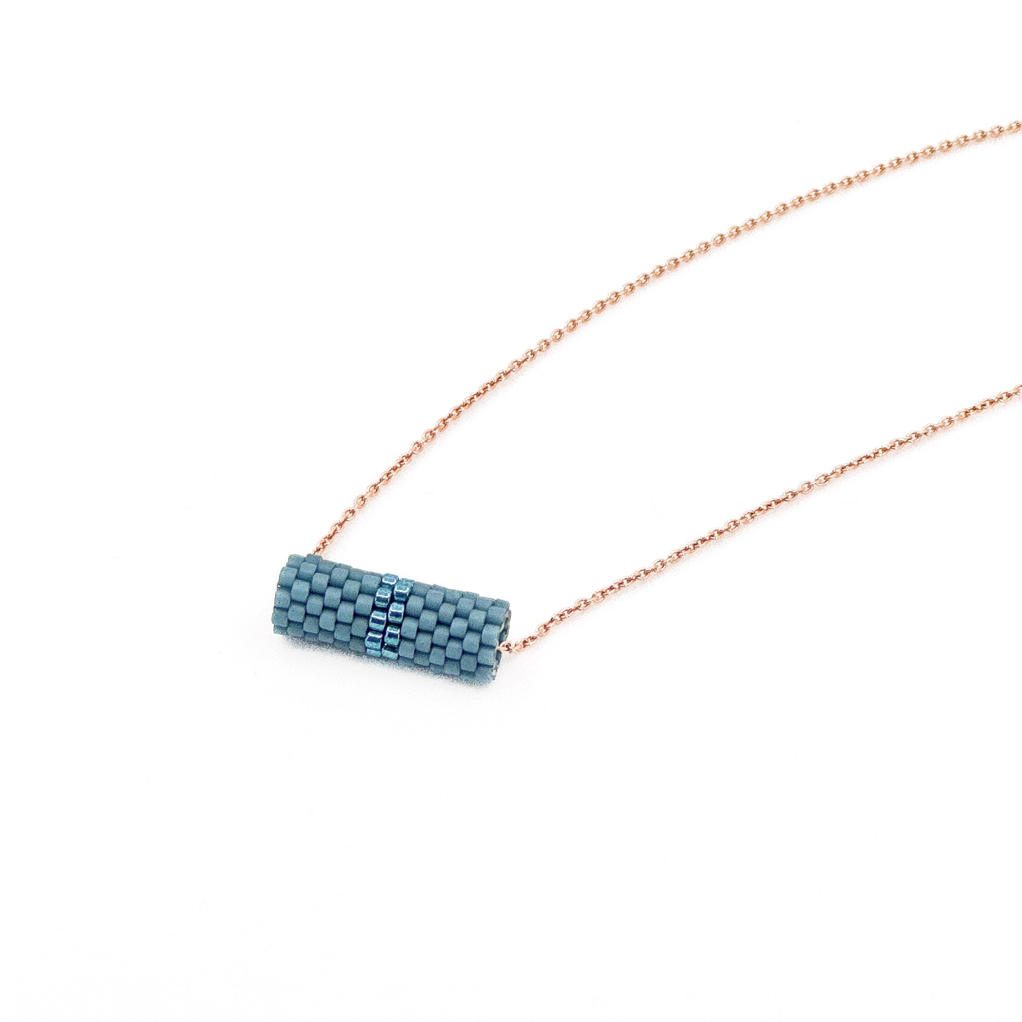 Blue beaded tube pendant necklace with rose gold chain and metallic center detail, slate blue beads, side view.