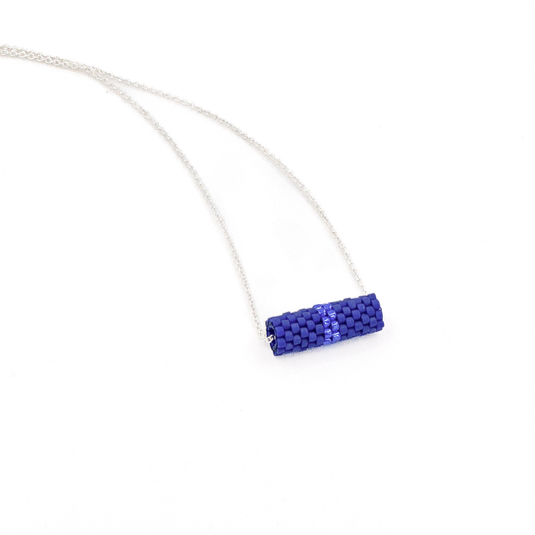Blue beaded tube pendant necklace with silver chain and metallic center detail, royal blue beads, side view.